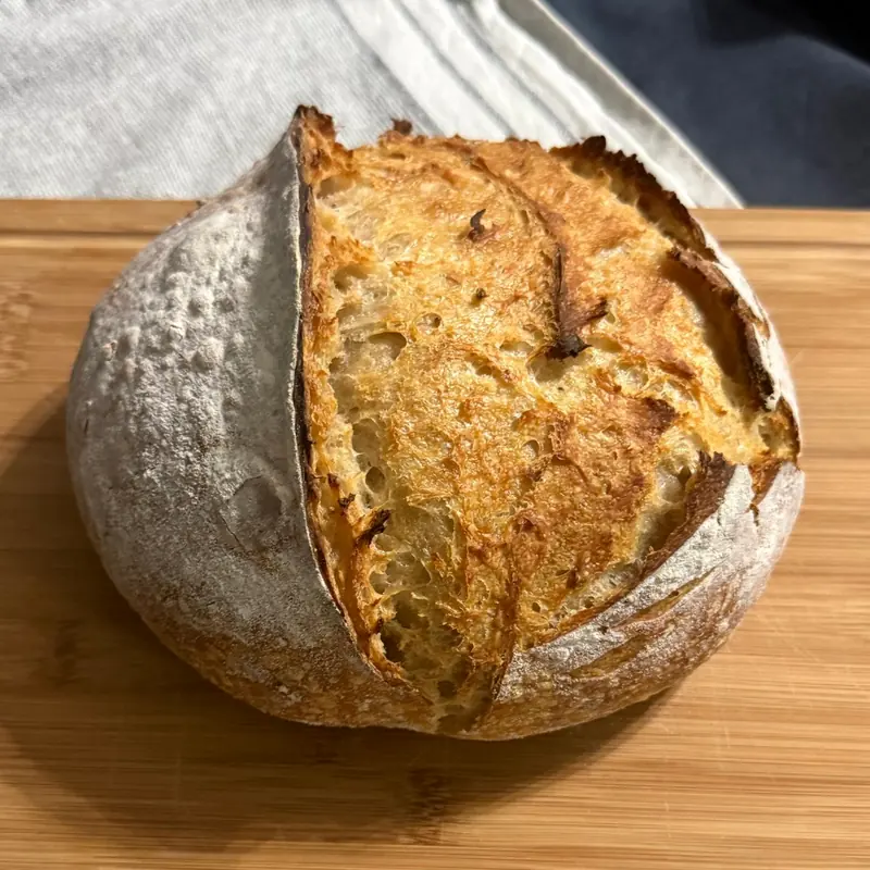 A sourdough loaf on a wooden board with a deep golden scored crust
