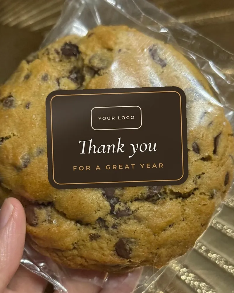 A wrapped cookie with a dark rectangular sticker reading Thank you for a great year, with space for a logo